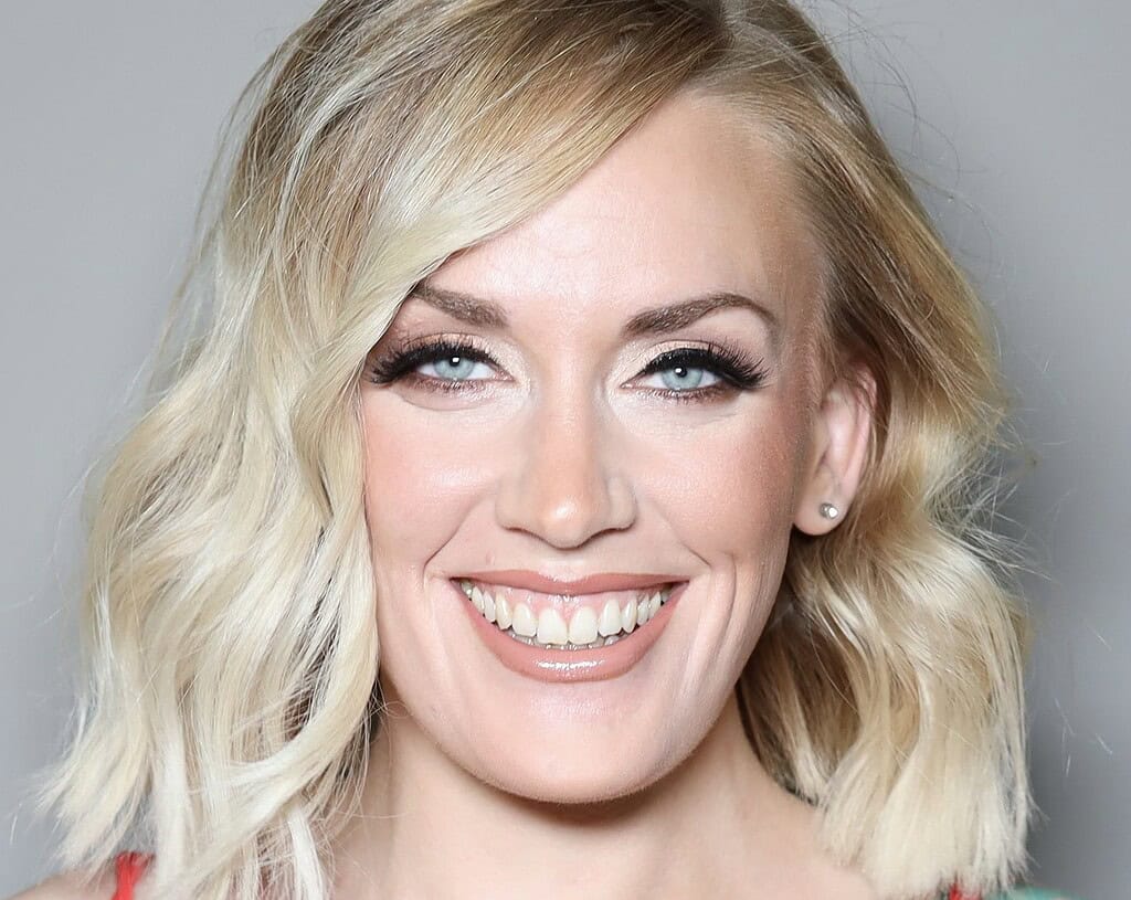 Smiling person with wavy blonde hair and makeup.